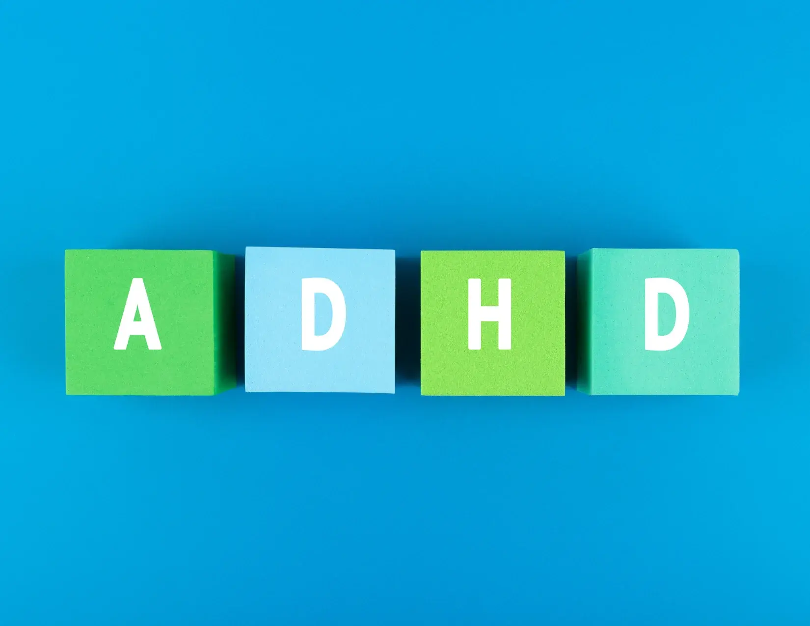 Four colored blocks on a blue background, each with a white letter spelling out "ADHD."