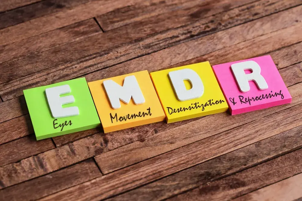Four colorful sticky notes on a wooden surface spell "EMDR," each labeled: Eyes, Movement, Desensitization, and Reprocessing.
