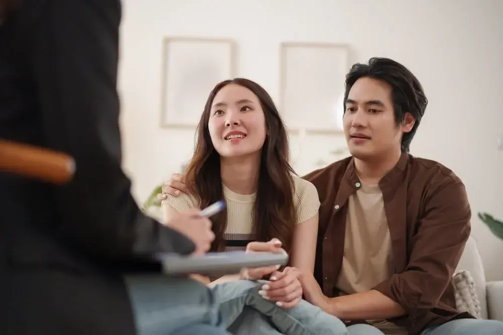 A couple sits close together, listening attentively to a pre marital counselor taking notes during a counseling session.