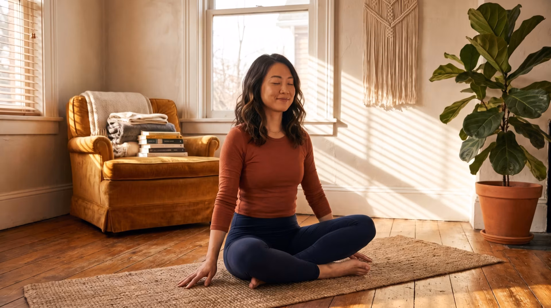 A woman in her thirties sitting cross-legged on a mat in her sunlit living room, one palm resting on the floor and eyes closed during a grounding practice.