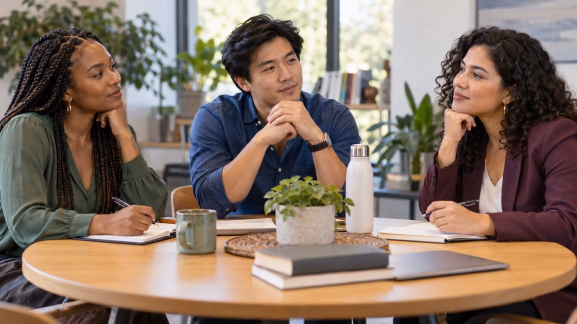 Three colleagues listen to one another around a table, practicing a culturally humble conversation.