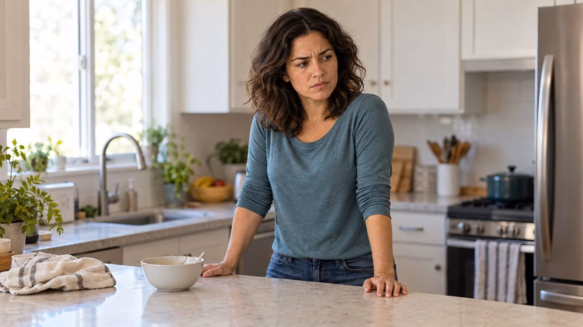 Woman at a kitchen counter with a tight jaw and furrowed brow, a moment of perimenopause rage after a small frustration