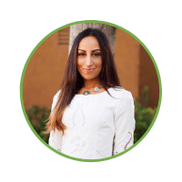 A woman with long dark hair, smiling, wearing a white embroidered blouse, and a turquoise necklace, stands in front of a blurred green background in San Francisco.