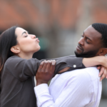 A woman is attempting to kiss a man, who is gently pushing her away with a disinterested expression, illustrating classic symptoms of rejection sensitive dysphoria.