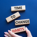 Four wooden blocks on a blue background arranged to form the phrase "Time to Change Habits," with hands holding the "Habits" block. These keystone habits can transform your life.