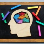 Silhouette of a head cutout on a chalkboard with colorful chalks inside and around it, symbolizing the diverse traits and creativity of neurodivergent minds filled with unique ideas.