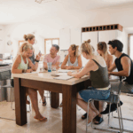 Seven people sit around a kitchen island engaged in conversation, writing, and drinking water in a bright, modern kitchen at a Behavioral Health Retreat near me.