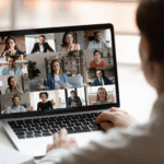 Person participates in an online bipolar support group video conference on a laptop, with nine people visible in separate windows on the computer screen.