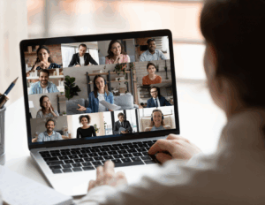 Person participates in an online bipolar support group video conference on a laptop, with nine people visible in separate windows on the computer screen.