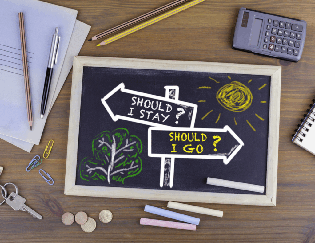 A chalkboard shows two directional signs labeled "Should I stay?" and "Should I go?"—a nod to couples considering divorce or seeking discernment counseling—with drawings of a sun and tree, surrounded by office supplies and coins on a wooden desk.