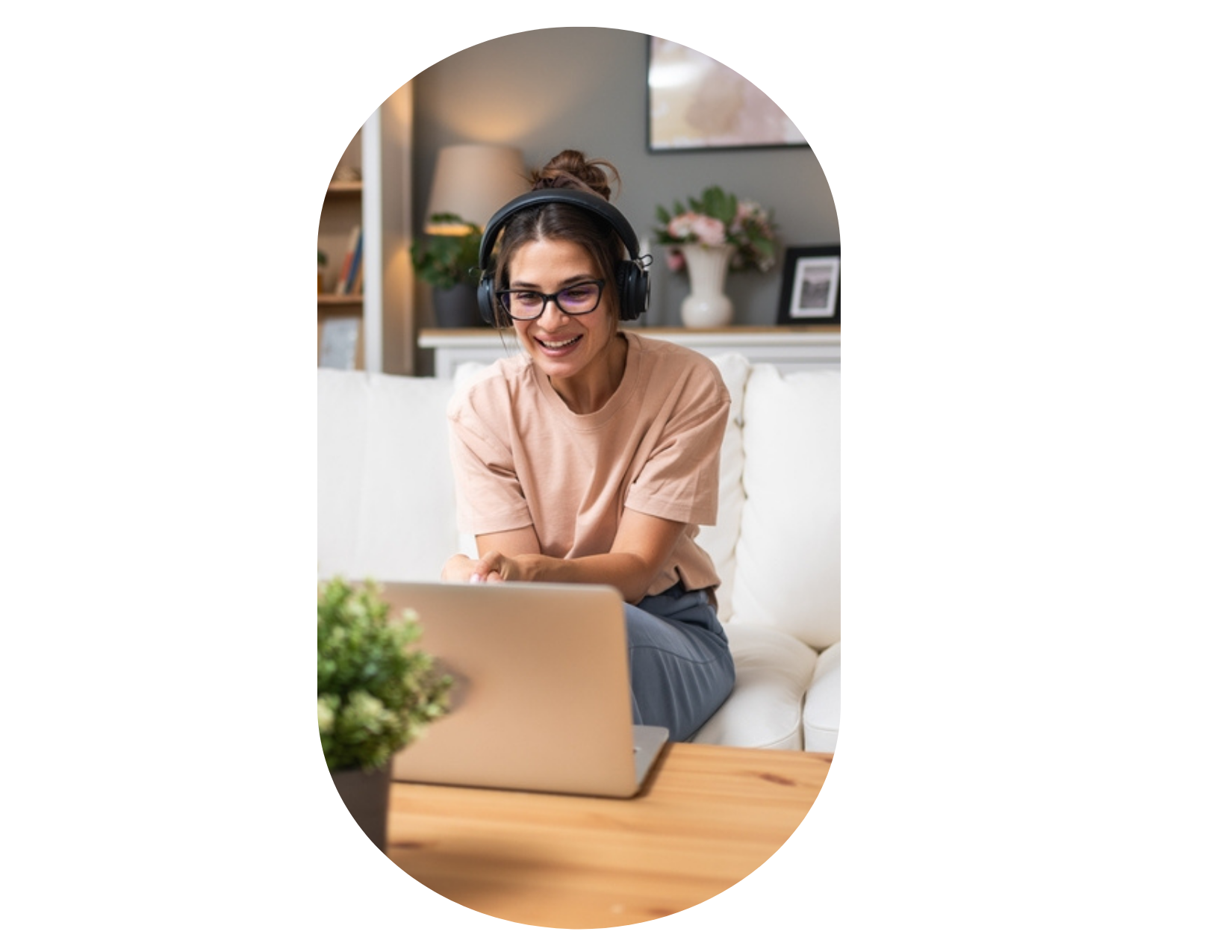 A woman wearing headphones and glasses sits on a couch, smiling at her laptop during a video call in her living room, possibly searching for health and wellness retreats near me to plan her next relaxing getaway.
