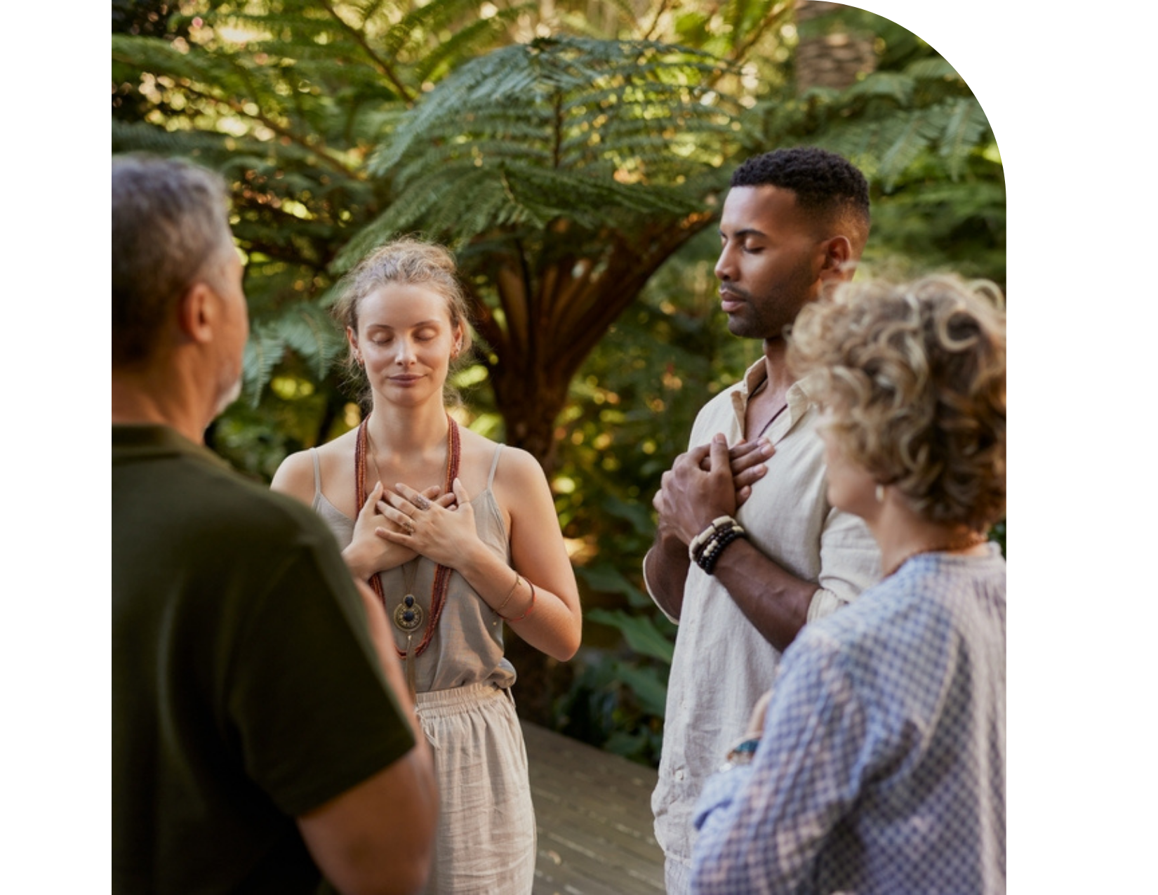 Four people stand in a circle outdoors with their eyes closed and hands on their chests, appearing to participate in a mindfulness or EMDR Therapy exercise.