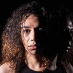 A person with curly hair faces forward, half of their face brightly lit, while their profile and reflection—hinting at hidden lurking trauma—are cast in shadow against a dark background.