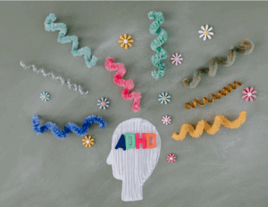 A drawing of a head with "ADHD" letters inside, surrounded by colorful pipe cleaners and flower decorations on a gray background—perfect for raising awareness about ADHD in adults and teens or promoting CBT therapy.