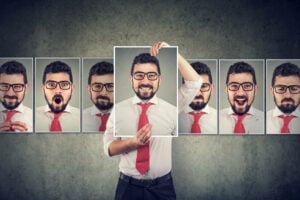 A man in a white shirt and red tie holds up a photo of himself smiling, surrounded by images of himself displaying various facial expressions—capturing the complexity of ADHD masking and the journey toward unmasking his true self.