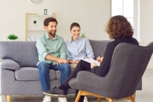 A couple sits together on a couch, smiling and holding hands, while talking to a professional during relationship counseling in Los Angeles.